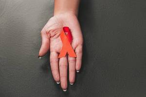 Red ribbon as symbol of aids awareness in hand on black background (Flip 2019)