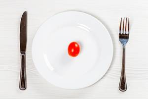 Red small tomato on a white plate with Cutlery. The concept of diet (Flip 2019)