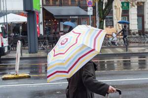 Regnerischer Tag - Dame mit buntem Schirm und Koffer auf dem Gehweg