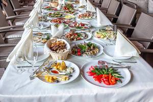 Reichgedeckter Restauranttisch: Weiße Tischdecke mit Besteck, Gläsern, Servietten und verschiedenen Arten von Lebensmitteln und Snacks