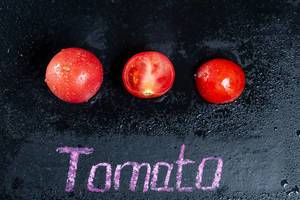 Reife Tomaten mit Wassertropfen auf schwarzem Hintergrund mit der Schrift Tomato
