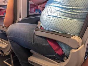 Reisepassagier mit Übergewicht im Flugzeug, sitzt eingeengt auf dem Sitz