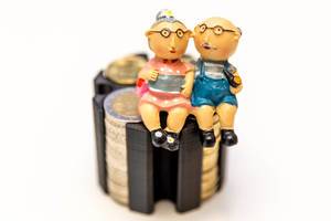Rentnerpaar auf gestapelten Münzen vor weißem Hintergrund - Altersvorsorge