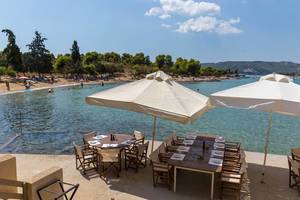 Restaurant-Terrasse "ΤΑΒΕΡΝΑ ΤΗΣ ΓΙΑΓΙΑΣ" am Meer, mit gedeckten Tischen unter quadratischen Sonnenschirmen
