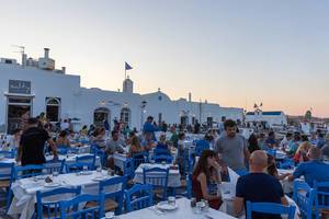 Restaurantgäste genießen Abendessen zum Sonnenuntergang an Hafen auf Paros, Griechenland