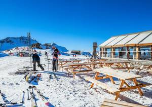 Restaurantterrasse mit Holztischen und -bänken in Skigebiet Vars in Frankreich mit Skifahrern und Skilift