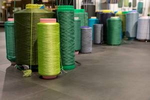 Riesige Spulen mit Faden in verschiedenen Farben stehen aufrecht auf Boden einer Fabrikhalle