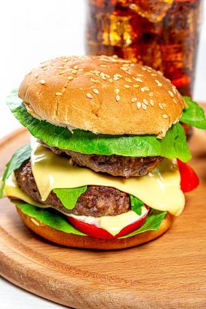Riesiger Burger mit zwei Fleischpatties, Salat und Käse, mit Eistee im Hintergrund