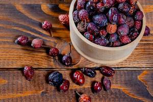 Ripe dried rosehip fruit in a bowl on wooden background
