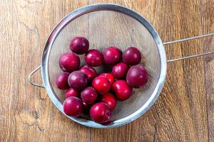 Ripe red plums in a sieve on a wooden table