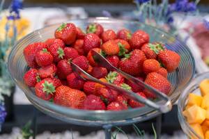 Ripe strawberries in a glass bowl with salad tongs