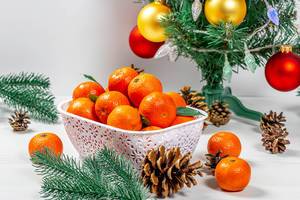 Ripe tangerines with cones and tree branches under a decorated Christmas tree