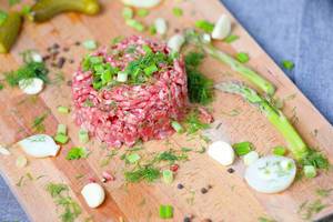 Rohes Rindfleisch: Zutaten für ein Beefsteak Tartare auf einem Holzbrettchen