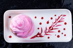 rosa Dessert mit pinker Creme und süßer Beerensoße auf weißem Teller