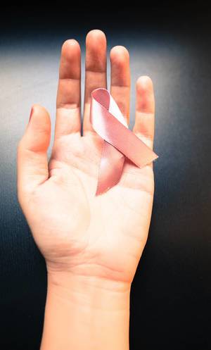 Rosa Schleife gegen Brustkrebserkrankung in der Hand einer Frau auf schwarzem Hintergrund