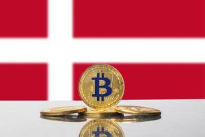 Rot-weiße Flagge Dänemarks mit Arrangement aus vier Bitcoin-Münzen im Vordergrund