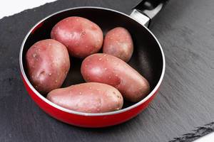 Rote Kartoffeln in kleiner Pfanne auf schwarzer Schieferplatte