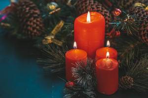Rote Kerzen neben Tannenzweigen zur festlichen Weihnachtszeit auf schwarzem Hintergrund