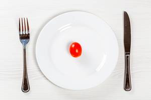 Rote kleine Tomate auf weißem Teller mit Besteck - Konzept der Ernährung