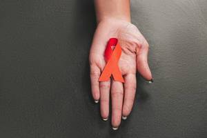 Rote Schleife als Symbol für Aids Bewusstsein in einer Frauenhand auf schwarzem Hintergrund