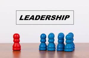 Rote Spielfigur vor Gruppe blauer Figur mit Überschrift LEADERSHIP steht für Führungskonzept