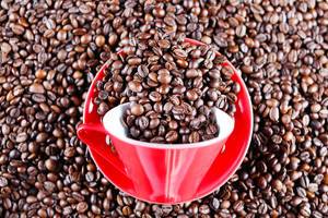 Rote Tasse mit Unterteller von Kaffeebohnen umgeben