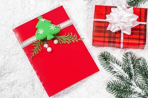 Rote Weihnachtsgrußkarte mit Geschenk und Tannenzweigen im Schnee