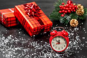 Roter Wecker mit Weihnachtsgeschenken, Tannenzweigen und Schneeflocken auf schwarzer Oberfläche