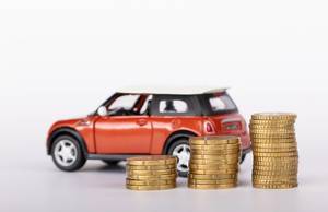 Rotes Spielzeugauto und Euromünzen gestapelt vor weißem Hintergrund