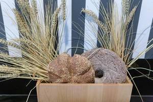 Rundes Sesam-Brot vor Weizenähren, als Landhaus-Dekoration, in einem Holzkorb