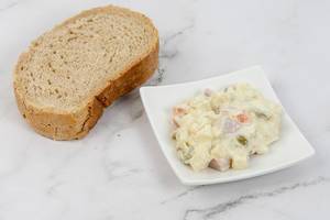 Russischer Salat neben einer dicken Scheibe Brot, auf einer marmorierten Oberfläche