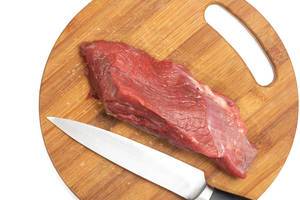 Saftiges Stück rohes Rindfleisch neben Fleischmesser auf hölzernem Küchenbrett isoliert vor weiß