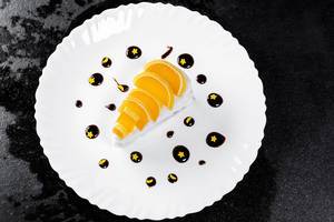 Sahniges Marmeladen-Kuchen Dessert mit Schokosauce und gelben Sternen verziert, vor schwarzem Hintergrund