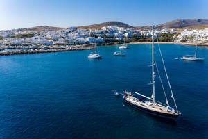 Sailboats and catamarans in the blue Aegean Sea water of bay Ormos Naousia, with typical greek houses in the background of Paros Island