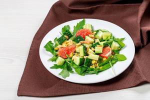 Salad with arugula, cucumbers, grapefruit and nuts on a white plate (Flip 2019)