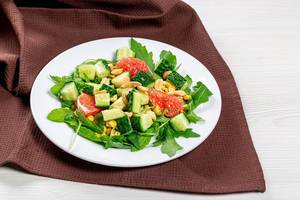 Salad with arugula, cucumbers, grapefruit and nuts on a white plate