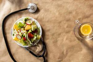 Salat aus frischem Gemüse mit Stethoskop und frischem Zitronenwasser als gesundes Ernährungskonzept