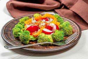 Salat mit Brokkoli, Radieschen, Paprika, Sesam- und Leinsamen im Teller mit einer Gabel