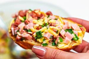 Sandwich with ham, cheese and green onions in a female hand close-up (Flip 2019)