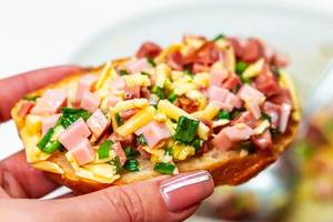 Sandwich with ham, cheese and green onions in a female hand close-up