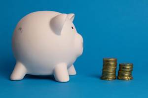 Saving money: two piles of Euro coins and a white piggy bank on blue background
