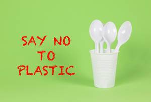 Say No To Plastic - Plastiklöffel im Becher auf grünem Hintergrund