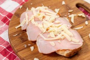 Schinkenscheiben und geriebener aromatischer Käse auf Brötchen auf hölzernem Küchenbrett