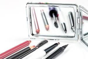 Schminkset: Kosmetikstifte und Eyeliner mit Spiegel im Hintergrund