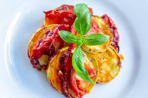 Schnelles Abendessen mit überbackenen Zucchini in Tomatensauce und garniert mit Basilikumblätter, auf einem weißen Teller