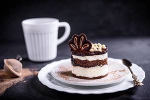 Schokoladen-Sahnekuchen mit artistischem Dekor auf weißem Teller und schwarzem Hintergrund
