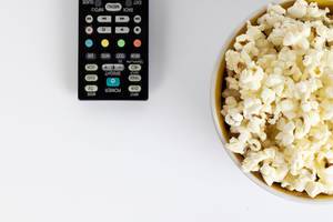 Schüssel mit Popcorn und Fernbedienung vor weißem Hintergrund