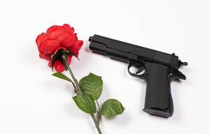Schwarze Handfeuerwaffe neben einzelner roter Rose vor weißem Hintergrund