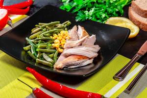 Schwarzer Teller, gefüllt mit gesundem Mittagessen: Spargel, Mais und gebackener Hühnerbrust