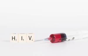 Scrabblesteine / Holzsteine ergeben das Wort HIV, neben einer Spritze mit Injektionsnadel